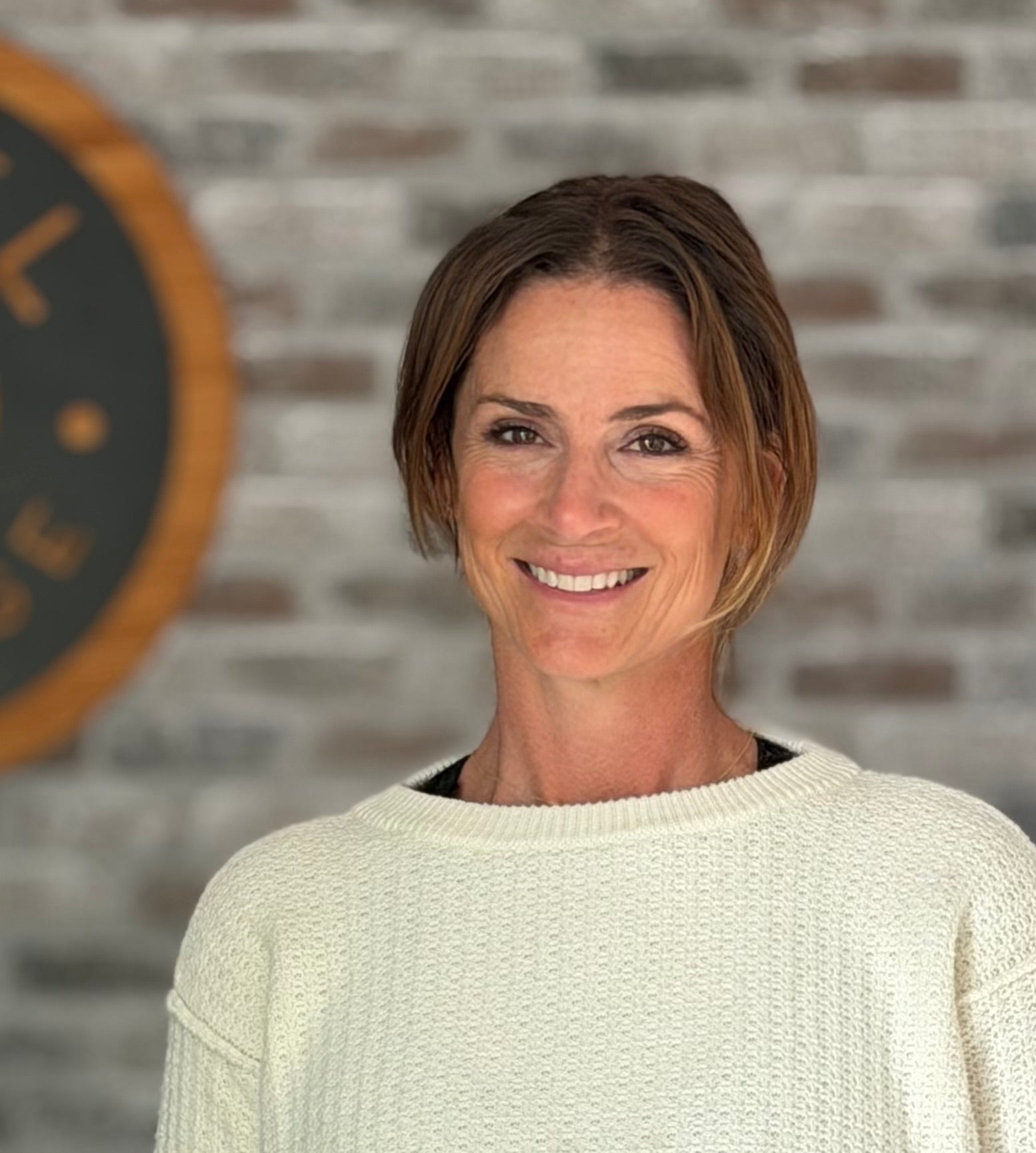 Jess in a white sweater standing in front of a brick wall with Rebel Massage logo.