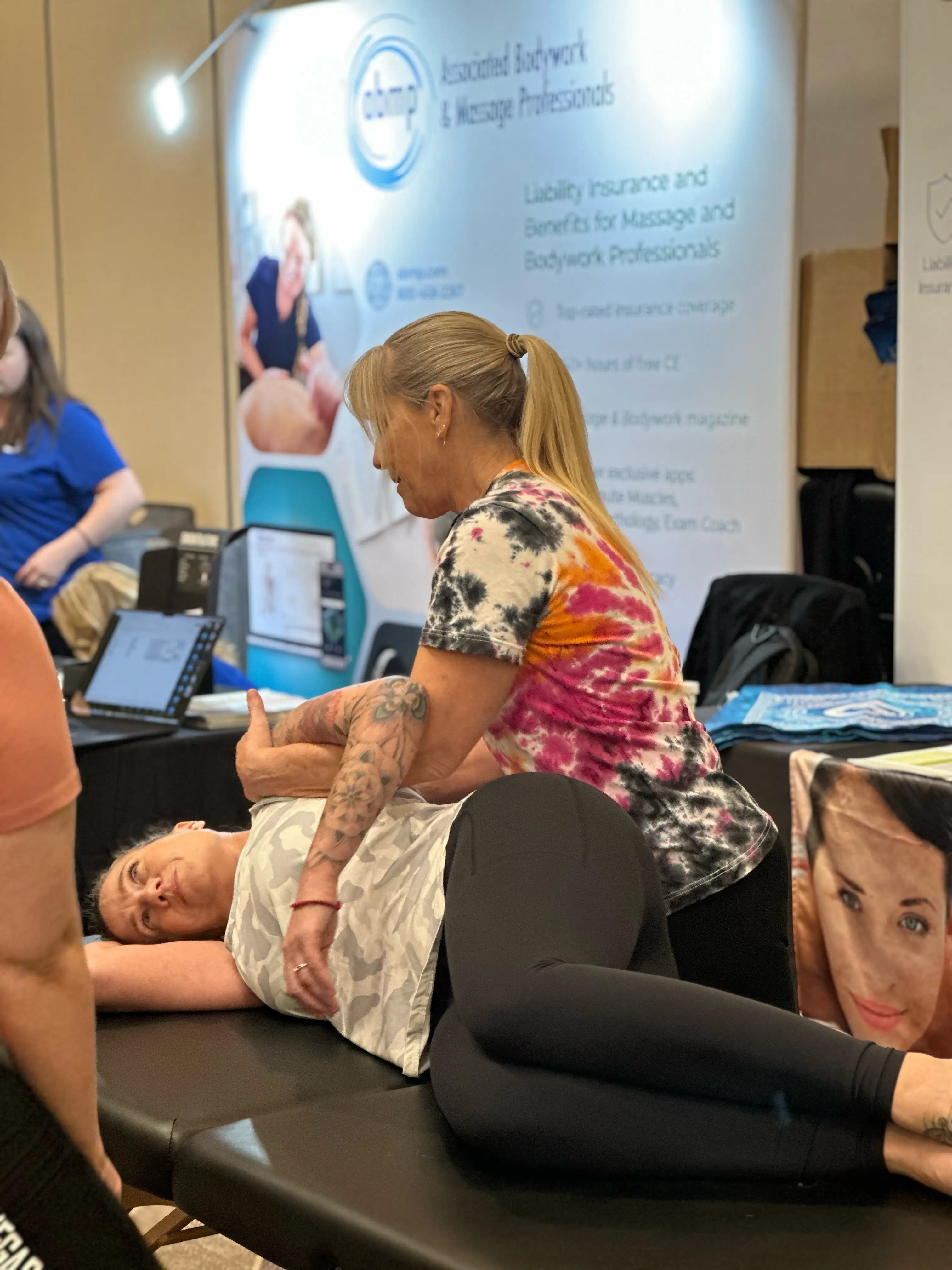 Allison providing massage demo to a person lying on a table at an ABMP event 