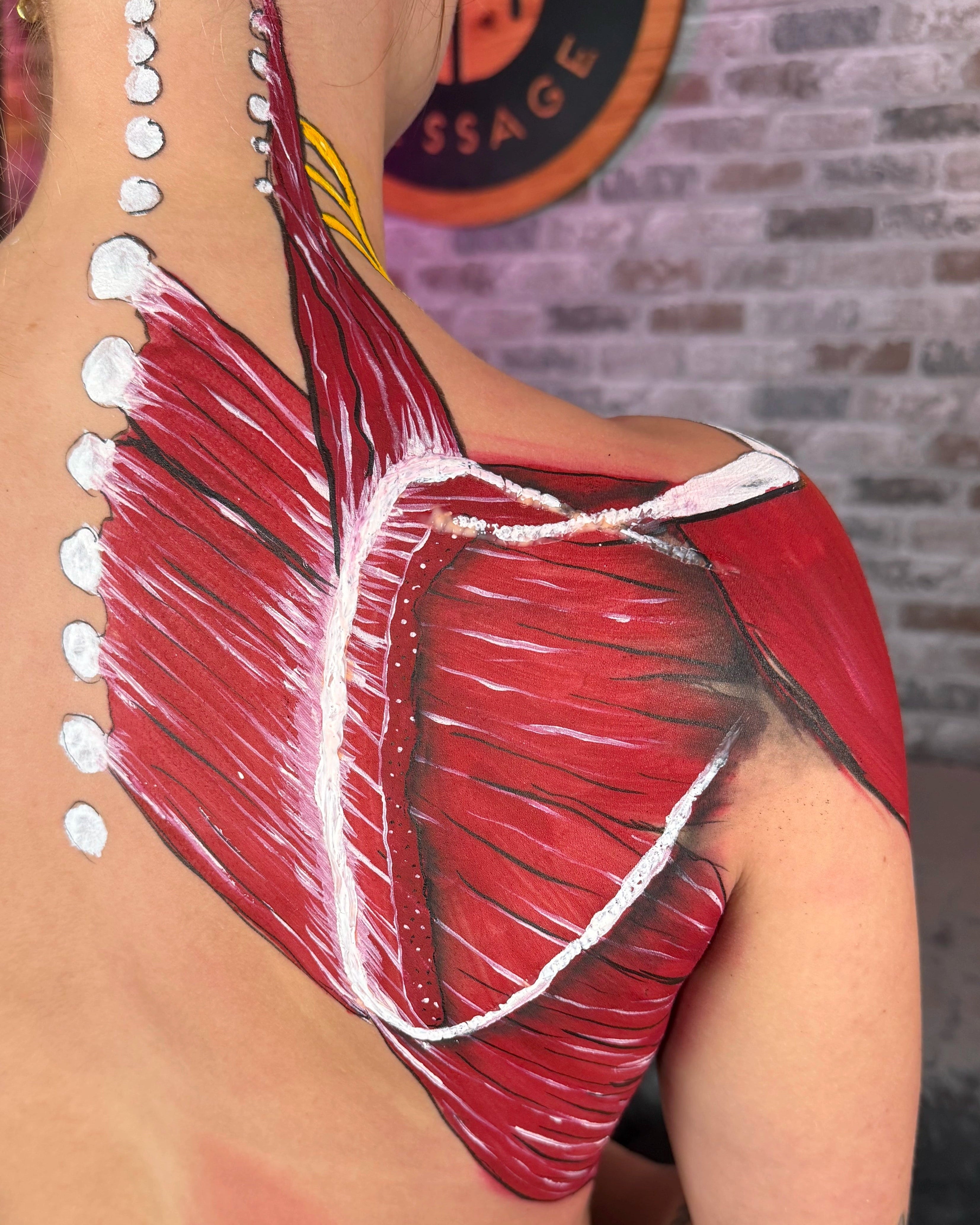 Artistic shoulder and back paint design with red and white colors on a person, against a brick wall background.